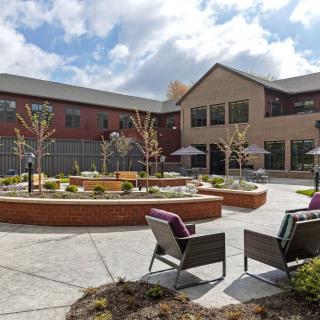A well-designed courtyard area with outdoor seating and landscaping in front of a modern building under a partly cloudy sky.