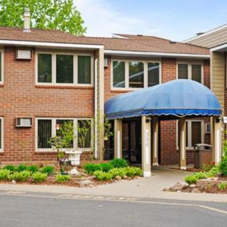 A brick residential building with a blue awning over the entrance, surrounded by greenery.
