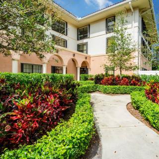 A well-maintained garden pathway leads to a modern, light-colored building surrounded by lush greenery and vibrant plants.