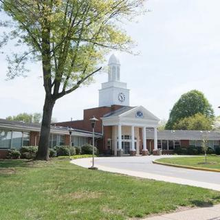 A colonial-style church building with a prominent white steeple, surrounded by trees and landscaping.