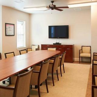 A modern conference room with a long table, multiple chairs, and a wall-mounted television.