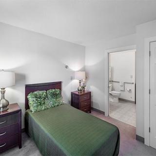 A minimalist bedroom with a single bed and green bedding, featuring two nightstands and lamps.