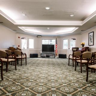 An empty conference room with arranged chairs, a television at the front, and an American flag.