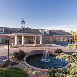 A stately brick building with a central fountain in the foreground, showcasing elegant architecture under a clear blue sky.