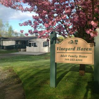 A vineyard sign with cherry blossoms in a lush spring landscape.