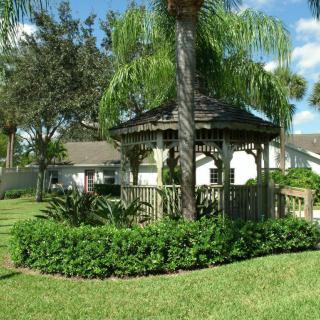 A charming wooden gazebo surrounded by lush greenery and palm trees in a sunny garden setting.