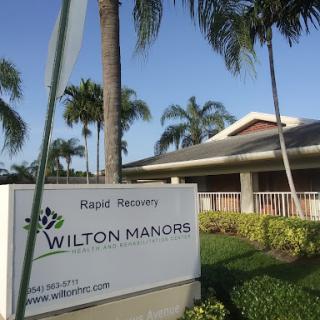 A view of the Wilton Manors facility sign surrounded by palm trees and well-maintained landscaping.