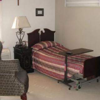 A cozy bedroom with a hospital bed, side table, and lamp.