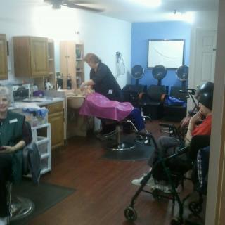 A busy hair salon where a stylist is attending to a client while others wait.