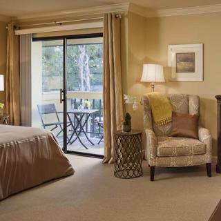 A cozy bedroom with a comfortable chair, lamp, and a view of the balcony.