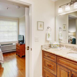 A cozy bedroom connected to a bathroom with wooden cabinetry and a well-lit mirror.