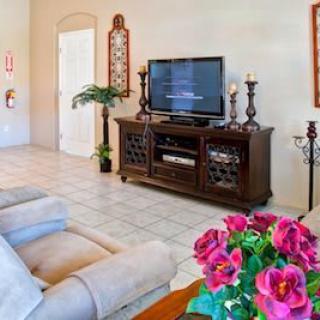 A cozy living room featuring a television on a wooden stand, cushy sofas, and vibrant flowers on the table.