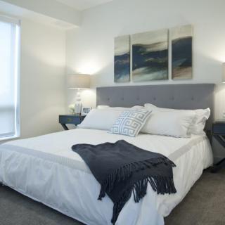 A modern bedroom with a neatly made bed, stylish decor, and soothing artwork on the wall.