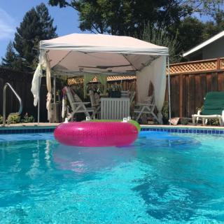 A sunny backyard pool scene with a pink inflatable ring and a cozy gazebo.