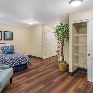 A cozy bedroom with wood flooring, featuring a bed and decorative elements such as a potted plant and an armchair.