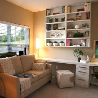 A cozy home office with a built-in desk and bookshelf, featuring a comfortable sofa and a window with natural light.