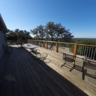 A spacious wooden deck with chairs and a table overlooks a scenic view under a clear blue sky.