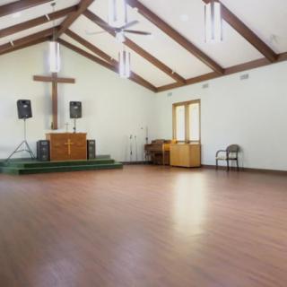 An empty church interior with a cross and altar on a wooden floor.