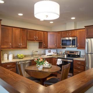 A cozy kitchen with wooden cabinets and a round dining table, featuring modern appliances.