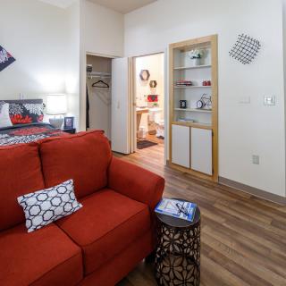 A cozy living room with a red sofa, decorative cushions, and wood flooring.