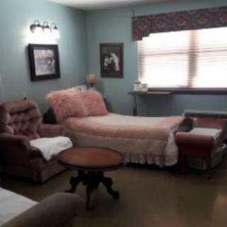 A vintage-style bedroom with a bed, armchair, and framed pictures on the wall.