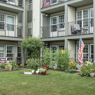 A view of an apartment building with balconies and a small garden adorned with flags.