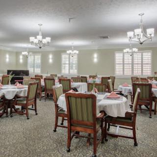 An elegantly arranged dining room with multiple tables and chairs, illuminated by chandeliers.