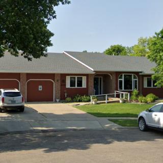 A suburban brick house with a well-maintained lawn and two cars parked in the driveway.