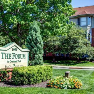 Entrance sign to The Forum apartment complex surrounded by lush greenery and well-maintained landscaping.