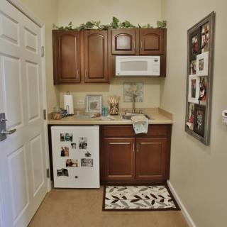 A compact kitchenette featuring wooden cabinets, a microwave, a small fridge, and decorative items on the counter.