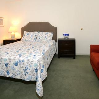 A cozy bedroom with a bed, nightstand, lamp, and a red couch.