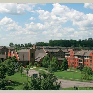 Aerial view of a campus with several buildings surrounded by trees and greenery under a partly cloudy sky.