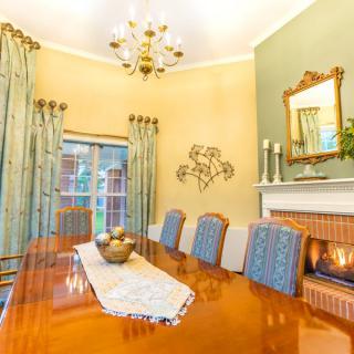 A cozy dining room with a polished wooden table, elegant chairs, and a warm fireplace.