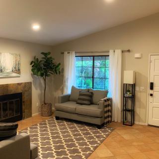 A cozy living room featuring a sofa, fireplace, and large window with curtains and a decorative rug.