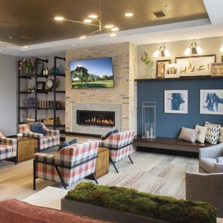 A cozy living room featuring a modern fireplace, plaid armchairs, and stylish shelving.