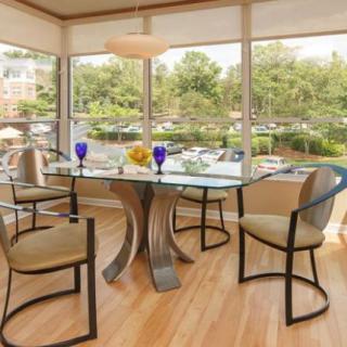 A modern dining room with a glass table and stylish chairs, surrounded by large windows that let in natural light.