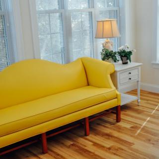 A bright living room with a yellow sofa and wooden flooring.