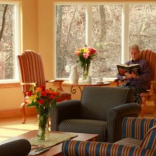 A cozy living room with comfortable seating, large windows overlooking the outdoors, and a person reading a book.