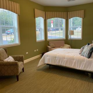 A cozy bedroom with green walls featuring a bed, armchair, and multiple windows allowing natural light.