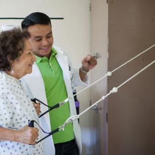 A healthcare professional assists an elderly woman during a physical therapy session.