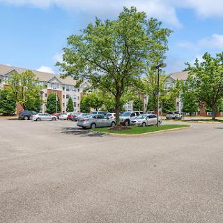 A peaceful residential parking lot surrounded by greenery and buildings under a partly cloudy sky.