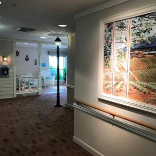 A brightly lit hallway in a nursing home featuring wall art and warm decor.