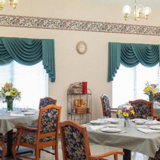 A well-decorated dining room with tables set for a meal, featuring floral arrangements and elegant curtains.