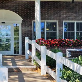 A charming entrance to a building adorned with vibrant flowers and a white fence.