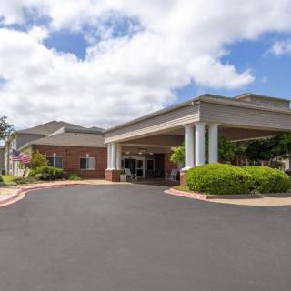 A well-maintained building entrance with a covered driveway set against a partly cloudy sky.