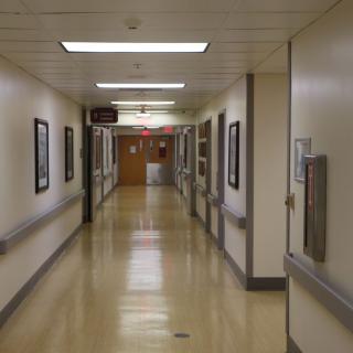 A quiet hospital corridor with fluorescent lighting and framed pictures on the walls.