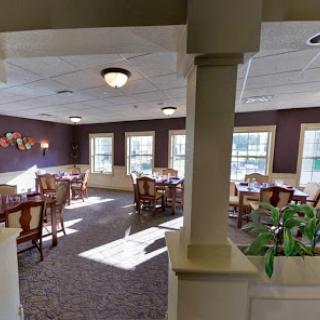 A cozy dining room setup with tables and chairs, illuminated by natural light from the windows.