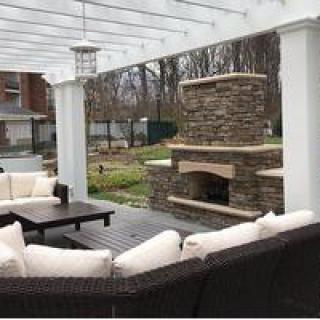 A cozy outdoor patio area with cushioned seating and a stone fireplace under a pergola.