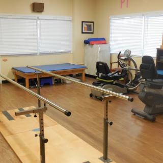 A well-equipped physical therapy room featuring rehabilitation bars and exercise machines.