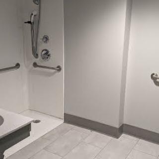 A spacious, accessible bathroom featuring a shower with grab bars and modern white tile flooring.